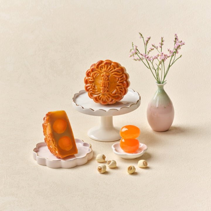 Three mooncakes on white stands with a vase of flowers on a beige background