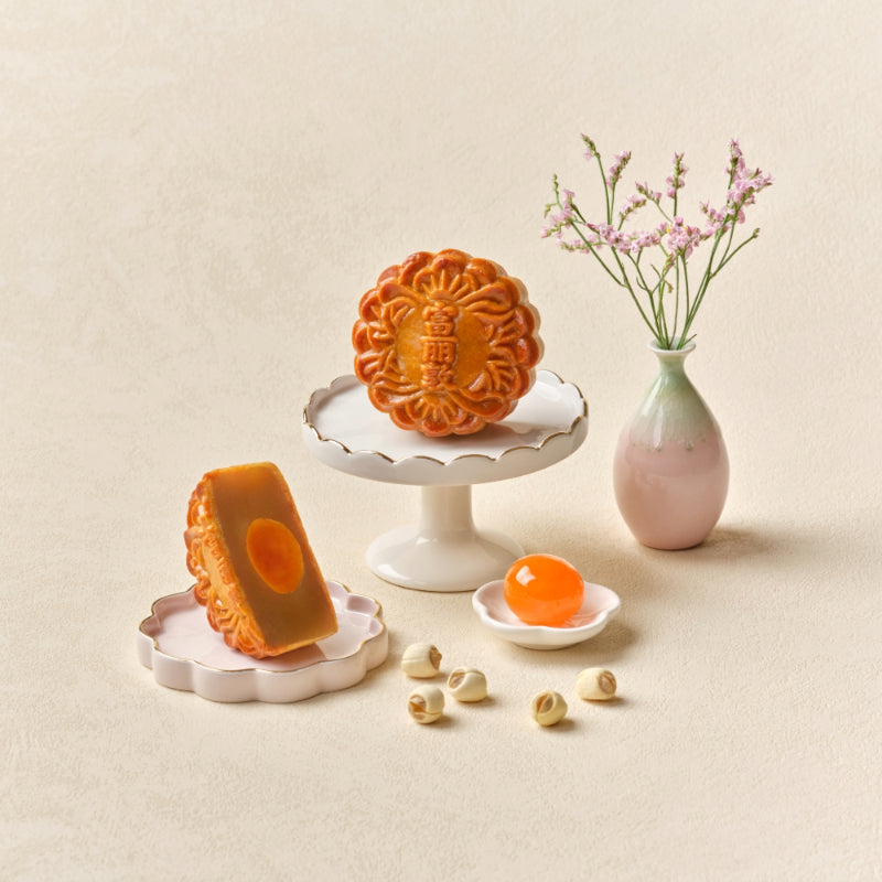 Two mooncakes on a decorative stand with a vase of flowers on a beige background