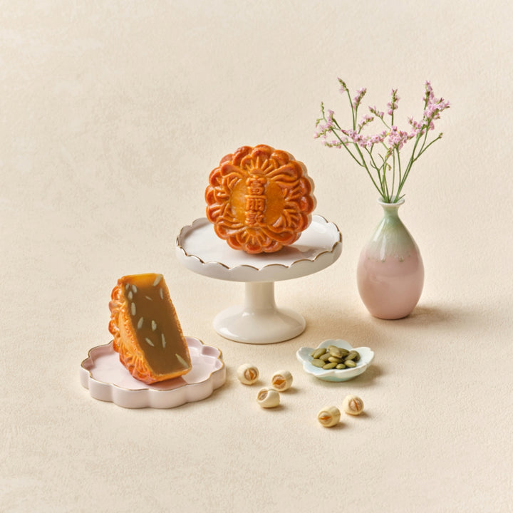 Two mooncakes on decorative stands with a vase of flowers on a beige background