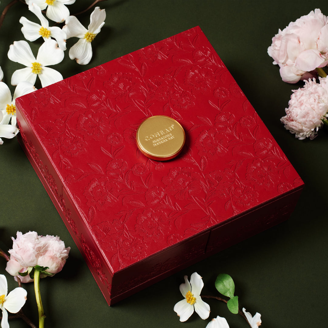 Red decorative box with a gold emblem on a dark surface surrounded by flowers