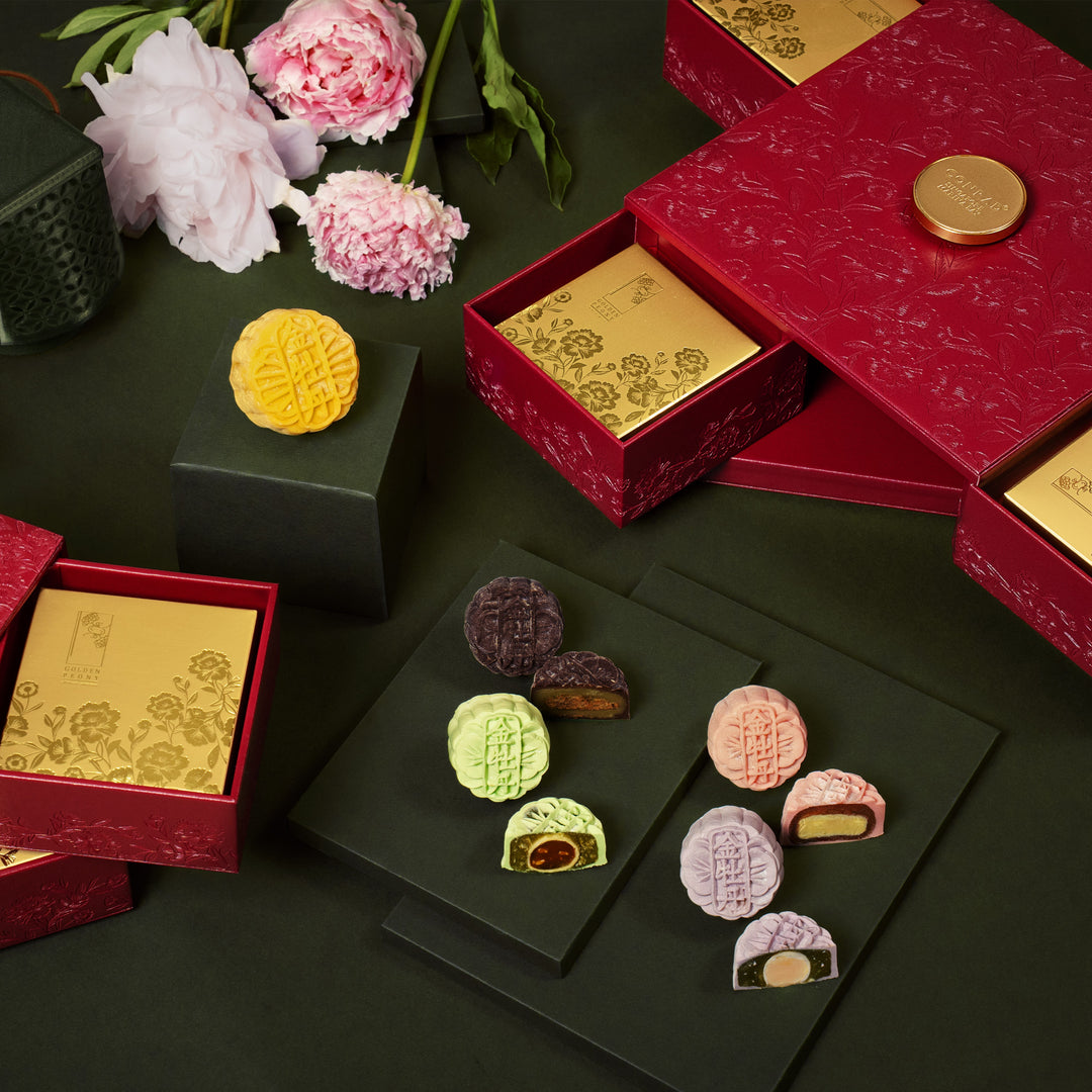 Decorative display of mooncakes in red and gold boxes with flowers on a dark surface.