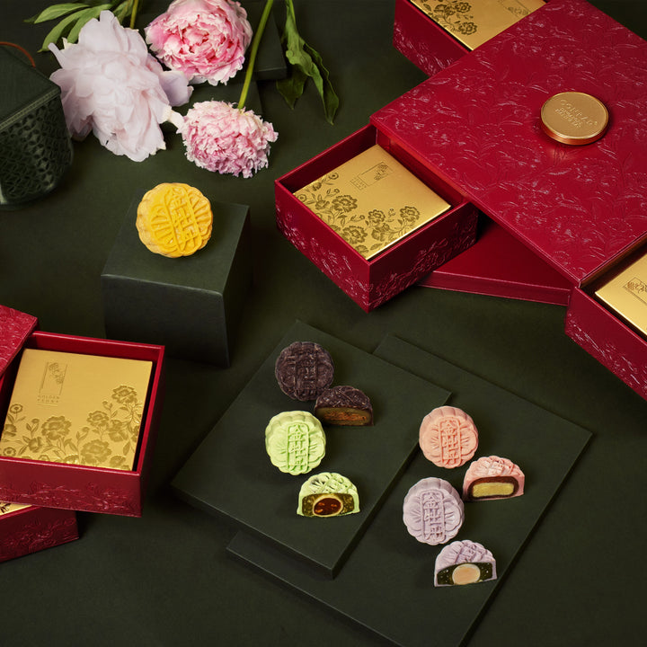 Decorative display of mooncakes in red and gold boxes with flowers on a dark surface.